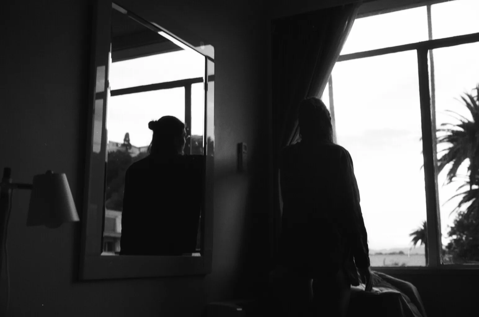 Woman staring out of window with reflection in mirror